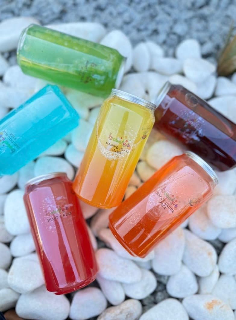 Colorful Boba Lush canned drinks on white pebbles